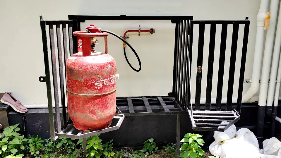 Photo of a gas cylinder placed inside a gas cage with a revolving trolley base and is connected to a gas pipeline.