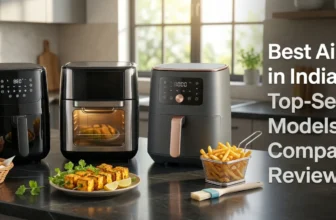A featured blog banner image for an article titled "Best Air Fryers in India (2026): Top-Selling Models Compared & Reviewed." The image displays three modern, distinct air fryer types side-by-side on a dark soapstone kitchen counter. On the left is a sleek black digital basket model, in the middle is a silver/black oven-style model with a glass window showing food inside, and on the right is a premium matte grey digital basket model with rose gold accents. Arranged invitingly in the foreground are baskets of golden-brown air-fried samosas, a plate of paneer tikka, and french fries, along with fresh produce and a basting brush. Natural light streams from a window in a modern Indian kitchen. Clean, bold text on the right reads: "Best Air Fryers in India (2026): Top-Selling Models Compared & Reviewed." Branding in bottom left corner: www.gascare.in.