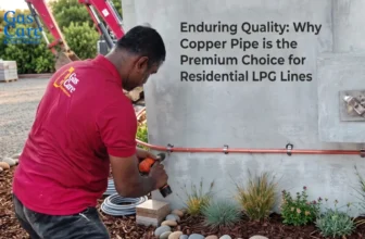 Gas Care technician wearing a red polo shirt uses a cordless drill to secure a horizontal red copper LPG pipeline with silver clips to a smooth concrete residential wall. In the detailed background, two red excavators and tidy green foliage are visible. Integrated text reads: Enduring Quality: Why Copper Pipe is the Premium Choice for Residential LPG Lines, with a gas care red and blue color logo in the upper left corner.