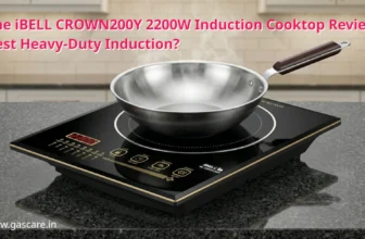 A detailed product review shot of the iBELL CROWN200Y 2200W Induction Cooktop, highlighting its sleek crystal glass surface with a stainless steel wok placed on the heating zone. Text on the image: iBELL CROWN200Y 2200W Induction Cooktop Review: Best Heavy-Duty Induction?, and in left bottom corner: www.gascare.in